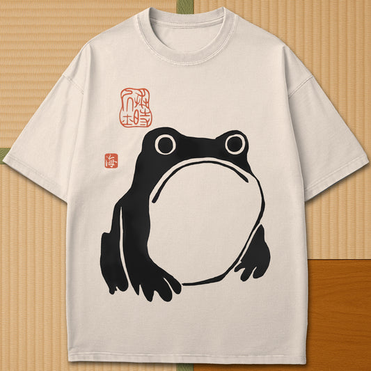 Japanese-inspired cotton Frowning Frog Print T-Shirt in Ivory on Comfort Colors 1717, styled in a modern flatlay scene.